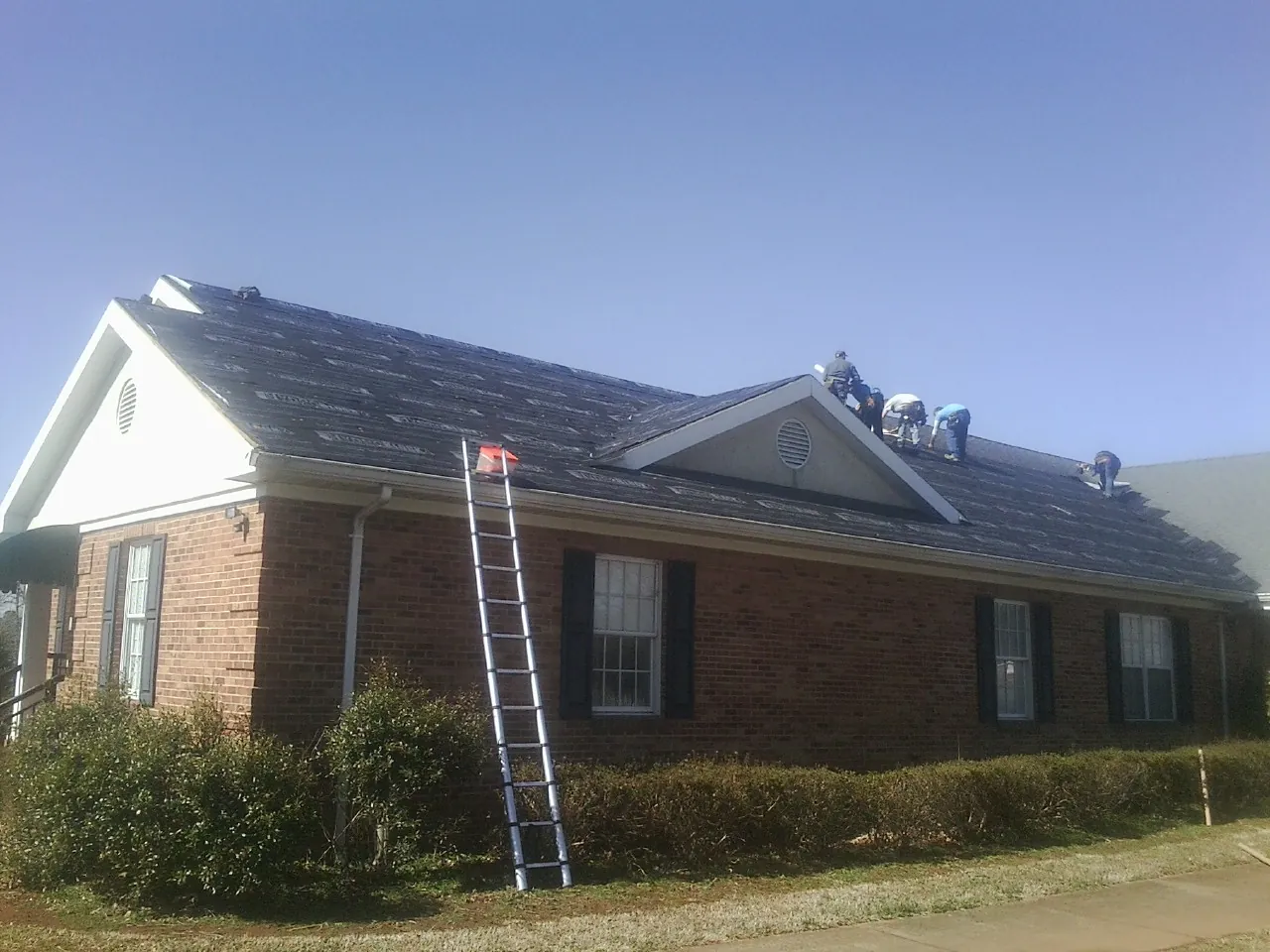 Crew tearing shingles off a brick ranch roof with a ladder set — Emergency Roof Repair work by our crew in Mohegan Lake