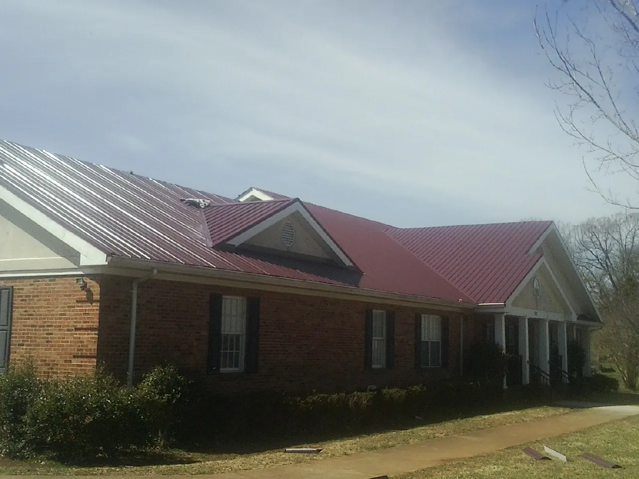 Red metal roof with gabled entries on a long brick building, from a Hail Damage Roof Repair job in Mohegan Lake