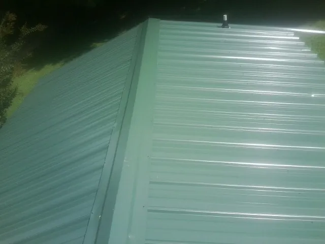 New green metal panels meeting at the ridge of a roof — Flat Roof Repair work by our crew in Mohegan Lake