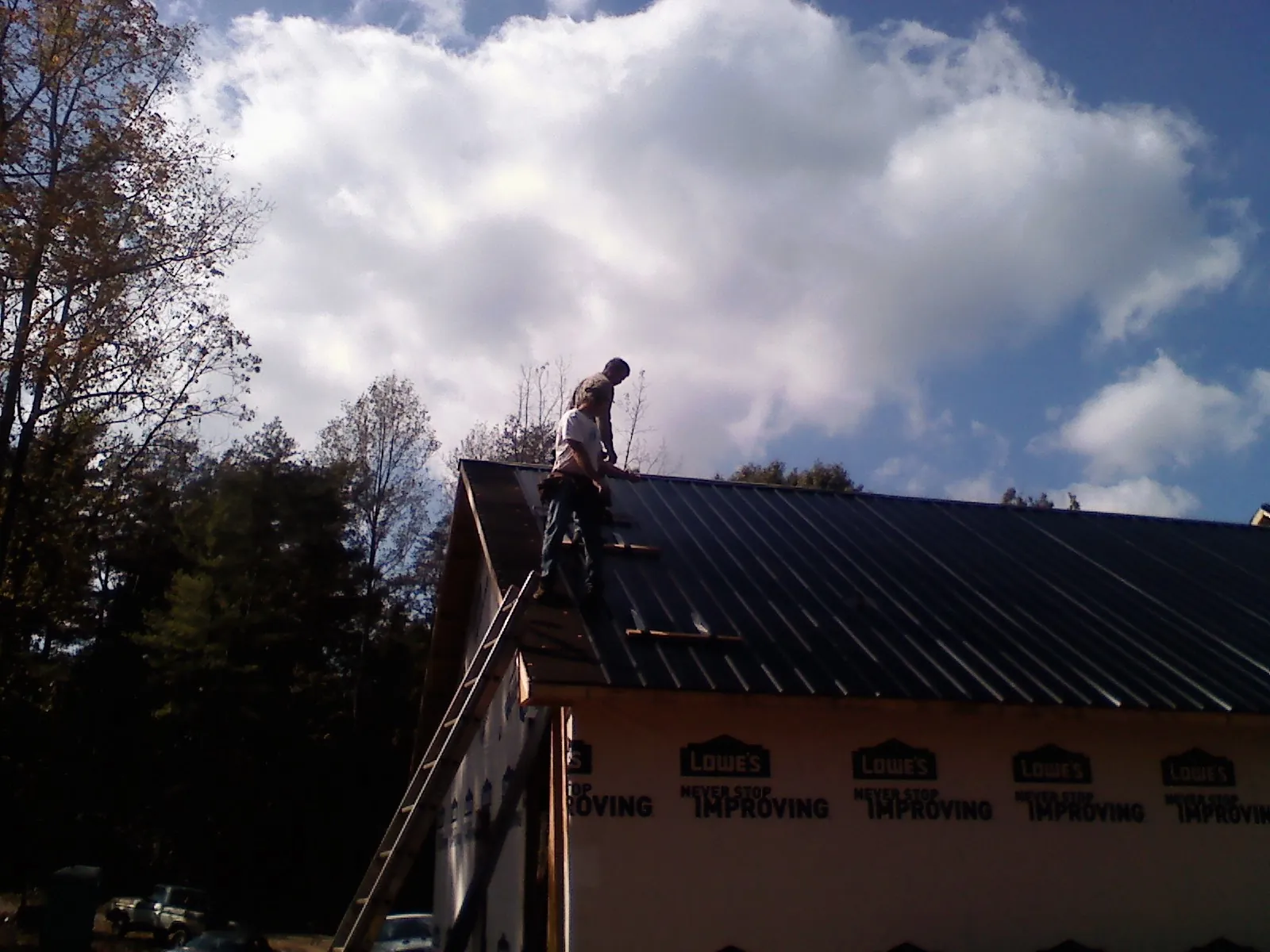 Roofer fastening dark metal panels high against a cloudy sky, from a Roof Inspection job in Mohegan Lake