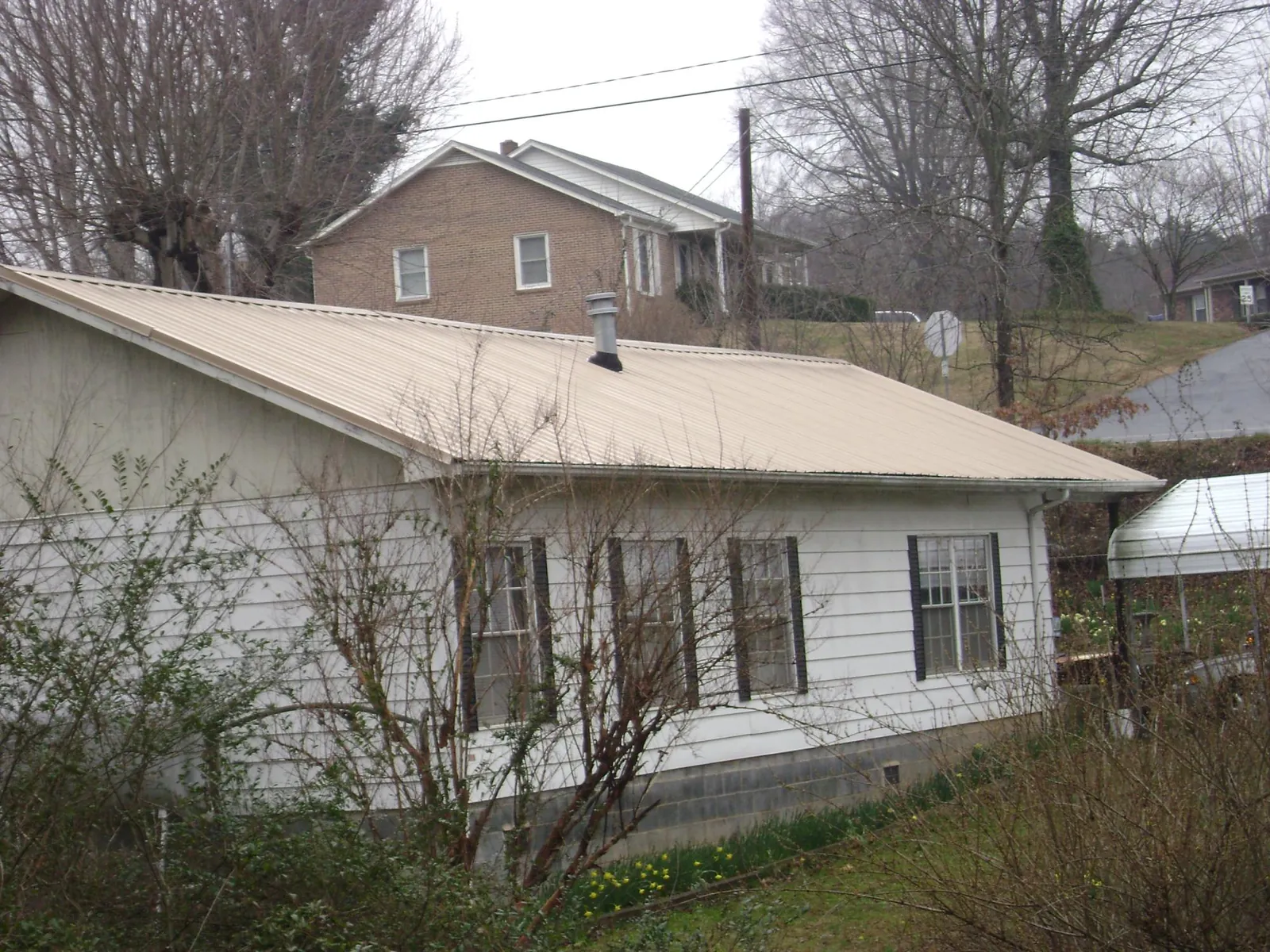 Tan metal roof on a white sided house set into a hillside — Commercial Roofing by Roofing Brothers in Mohegan Lake